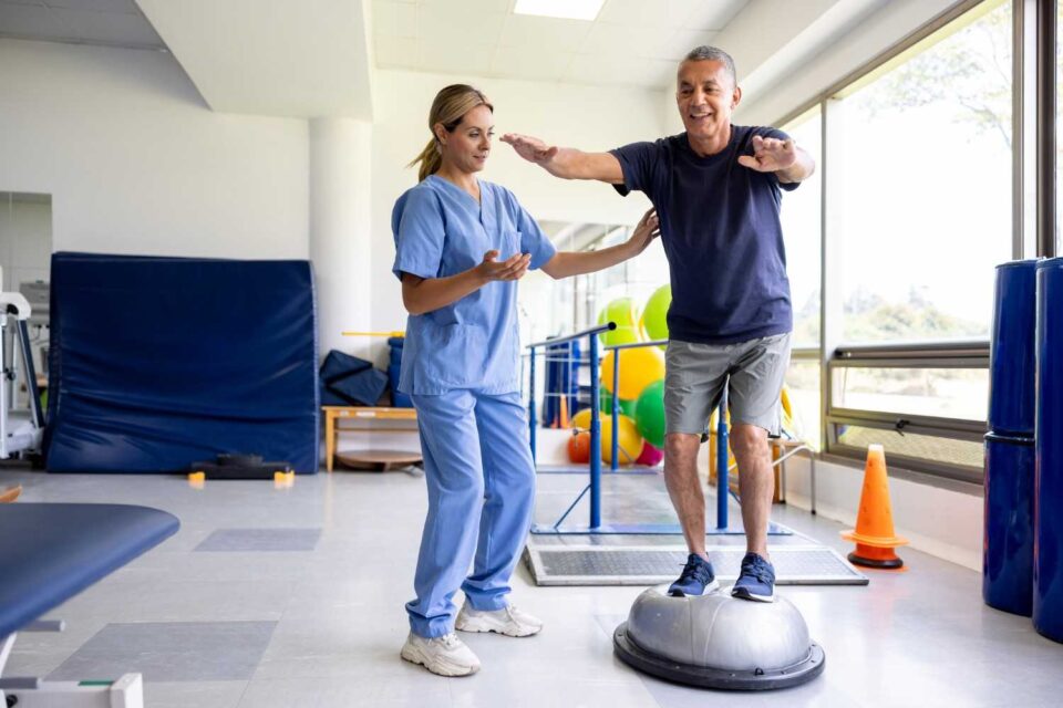 Person balancing on a bosu ball with therapist guidance in a physical therapy clinic