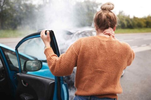 Women standing by smoking car, holding neck after apparent roadside breakdown