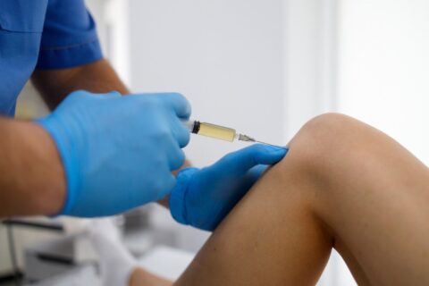 Medical professional administering an injection into a patient's knee in a clinical setting