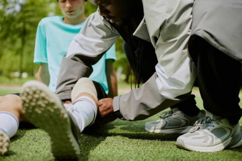 Coach wrapping athlete ankle during outdoor sports training session on grass