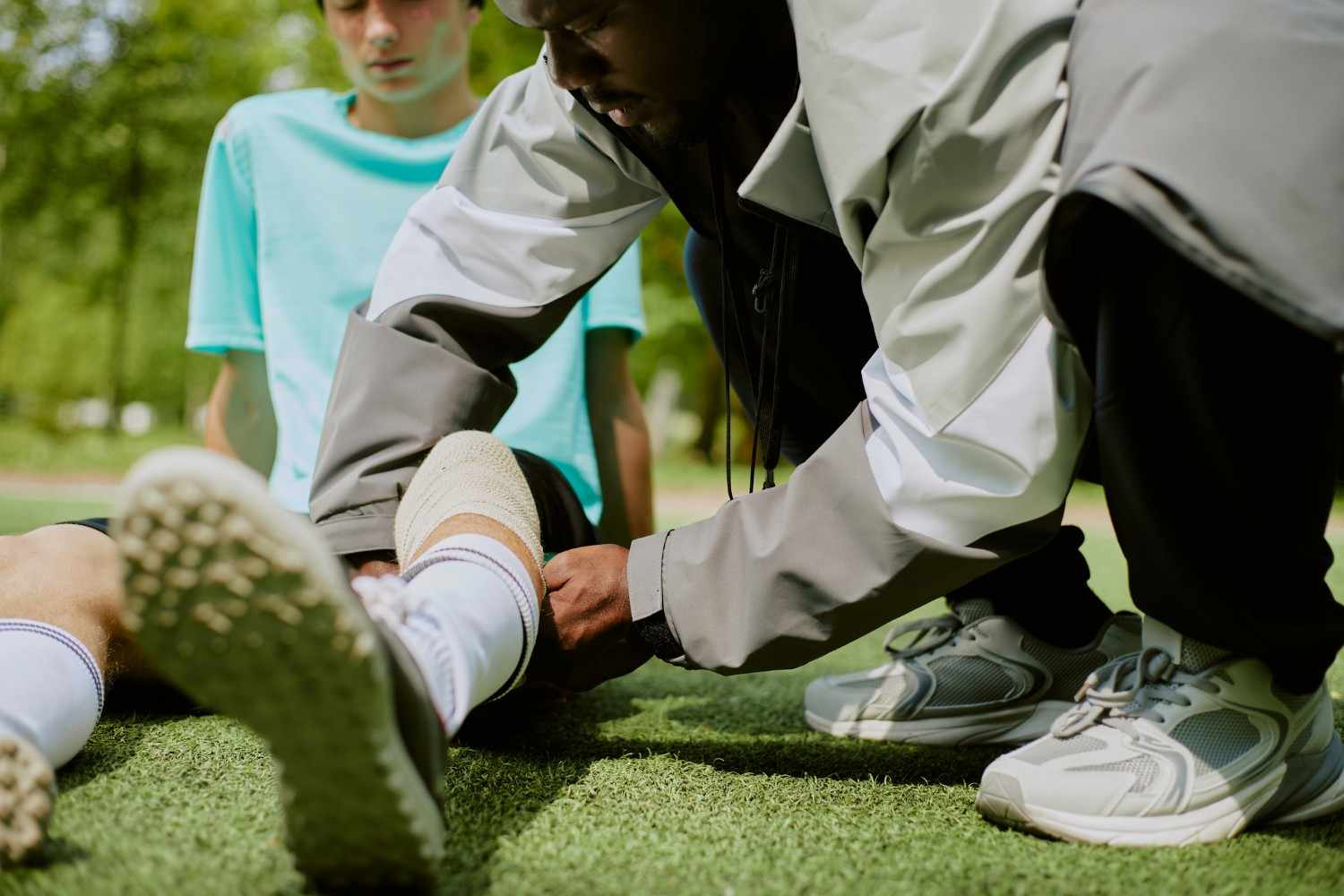 Coach wrapping athlete ankle during outdoor sports training session on grass